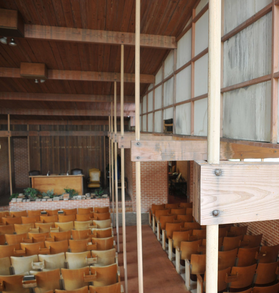 Church interior featuring exposed red brick and exposed wooden beams, with individual wooden seats (not pews).
